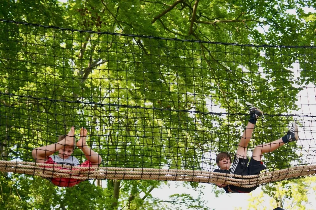 Two boys sitting and laying in a Hammock-Style Treetop Walkway netted bridge