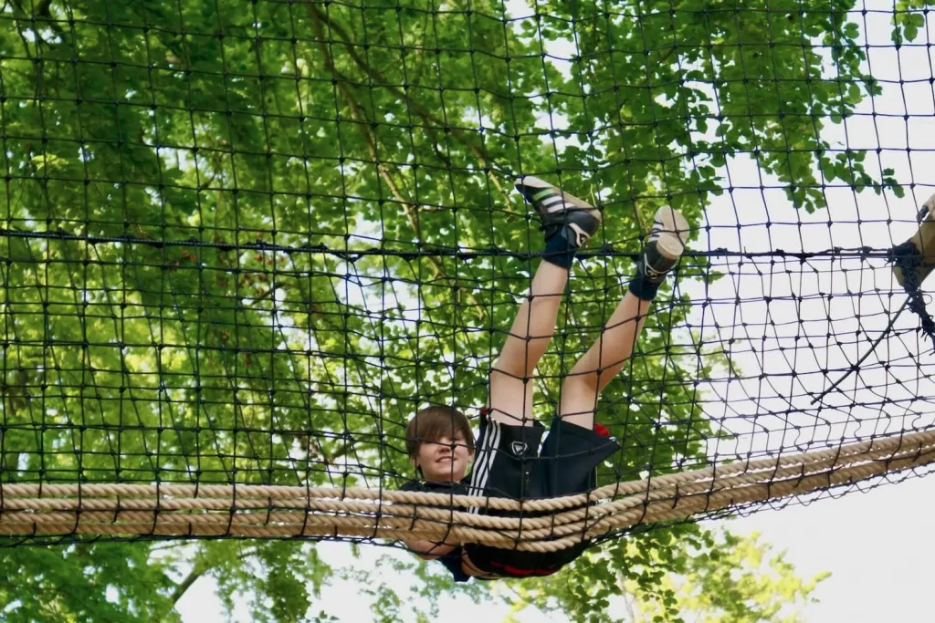 Boy sitting and laying in a netted Treetop Walkway in the trees.