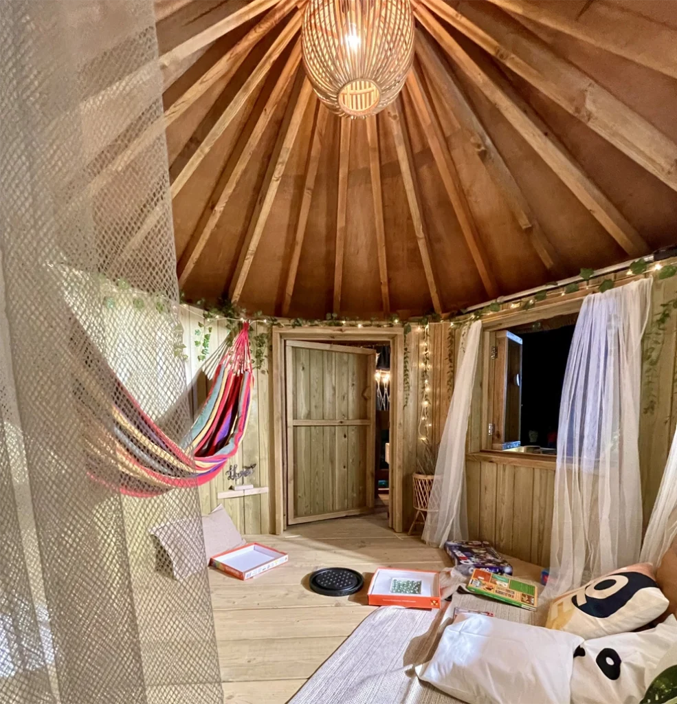 Inside playful treehouses with curtains, rugs, cushions, hammock, light in the ceiling and fairy lights around the wall.