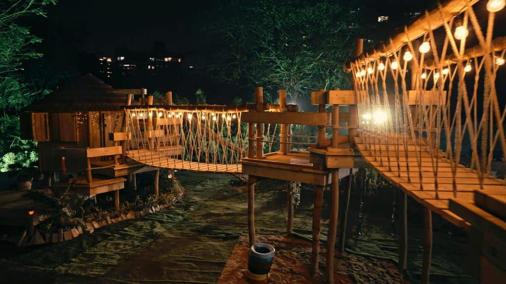 Treehouse project at night with a Treehouse, two Rope Bridges joined by a Deck Platform, there are fairy lights across both Rope Bridges.