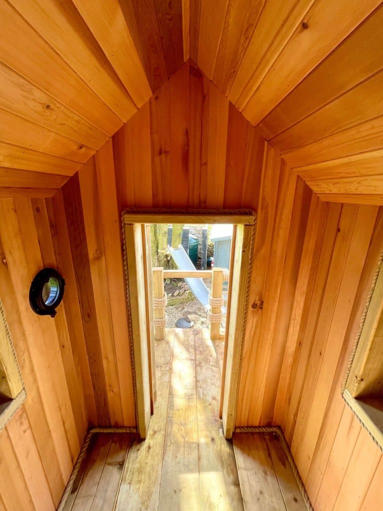 Inside of Treehouse made from Cedar Timber with walls roof and door opened to view stainless steel Slide