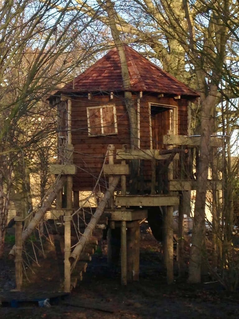 Kids Treehouse in wooded garden in Cedar with crooked windows and door.