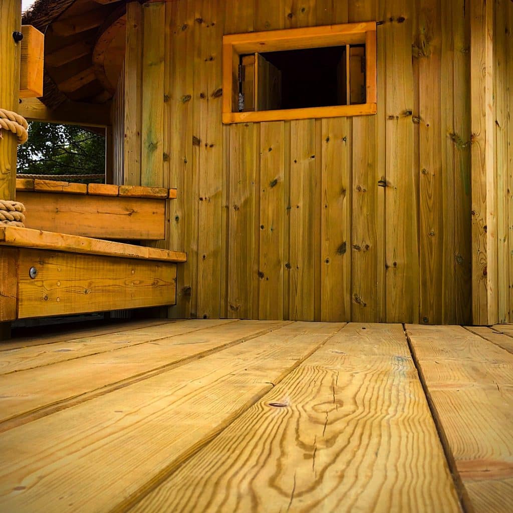 A treehouse deck showing two timber steps and the exterior wall of a garden treehouse.