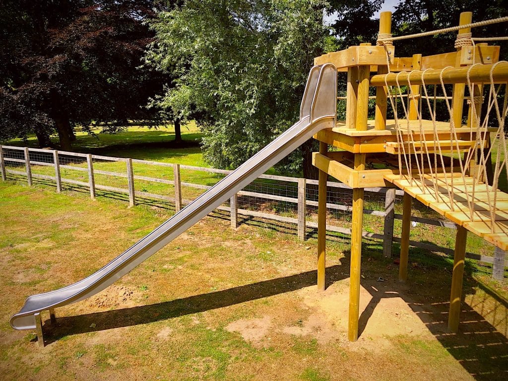 Stainless steel garden slide as part of treehouse and rope bridge.