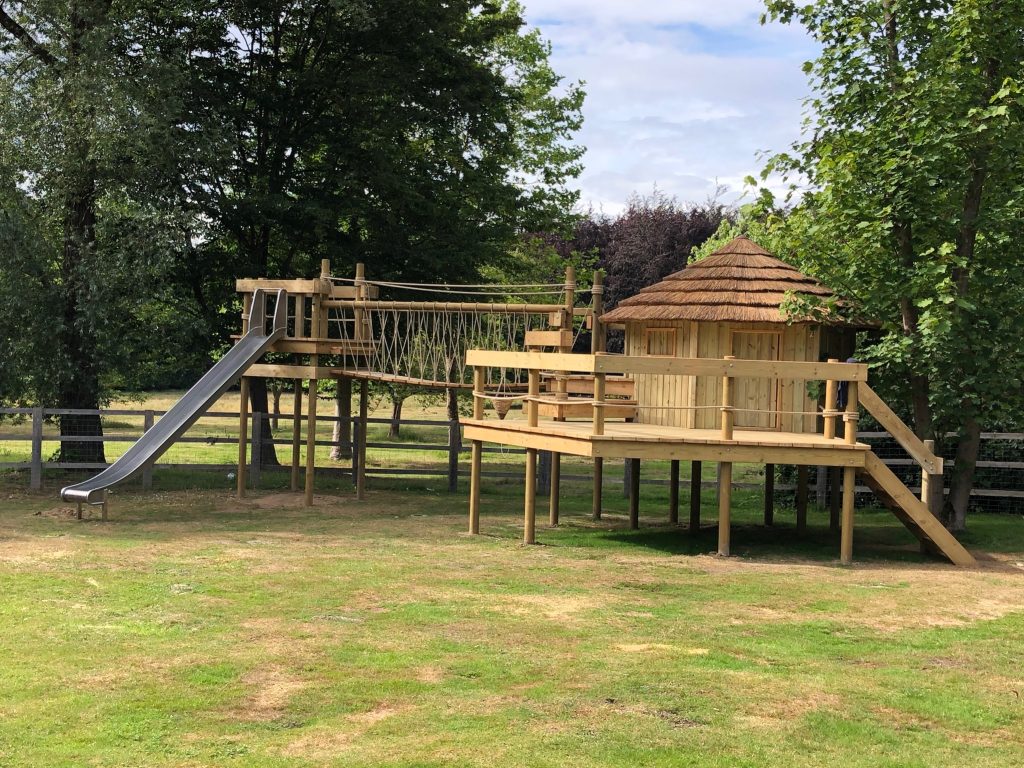 A garden treehouse with added extra treedeck, rope bridge and high stainless steel slide in a large summer garden in Ottershaw, Surrey.