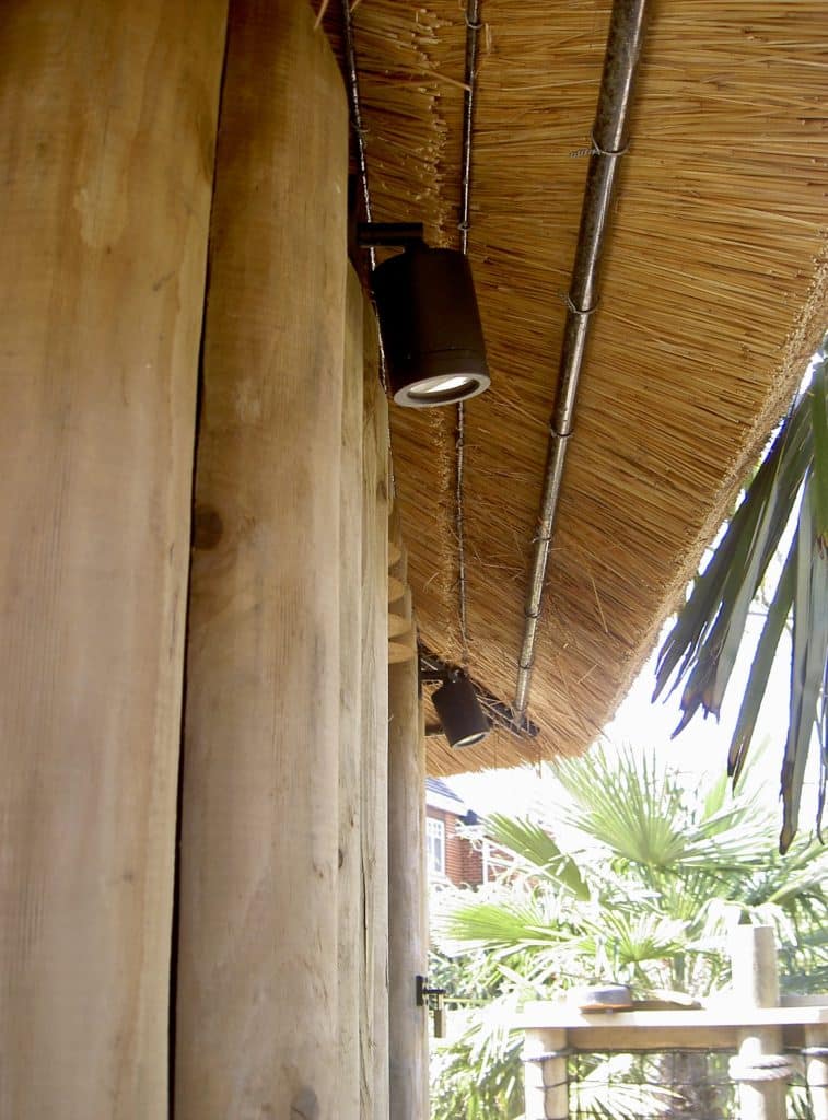 The underside of this thatched roof garden treehouse is surrounded by outdoor lights which are fixed facing downwards from the roof to provide illumination at night time.