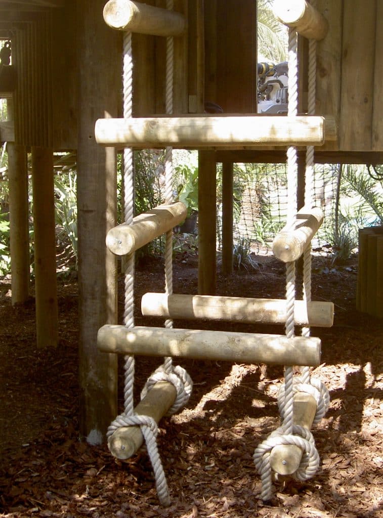 A chunky four sided rope ladder leads up to a deck in a landscape garden treehouse