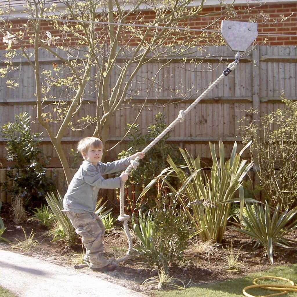 A small boy pulls back a rope on his garden zip wire